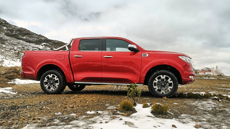 Vista lateral de camioneta automatica POER color roja estacionada sobre terreno rocos con nieve.